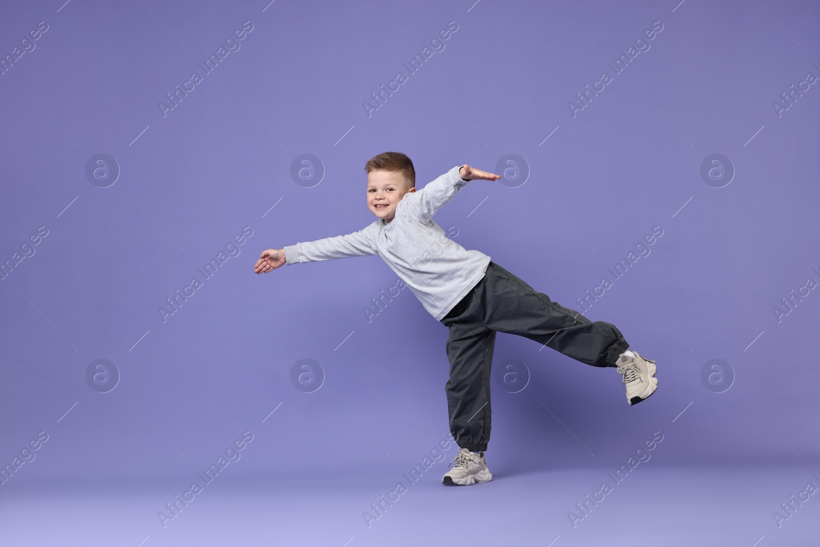 Photo of Happy little boy dancing on violet background