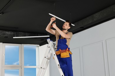 Electrician in uniform installing ceiling lamp indoors