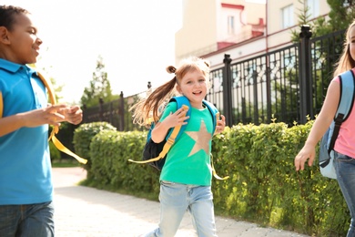 Photo of Cute little children with backpacks running outdoors. Elementary school