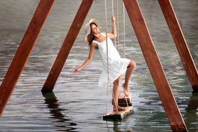 Photo of Young woman on swing over water on sunny day