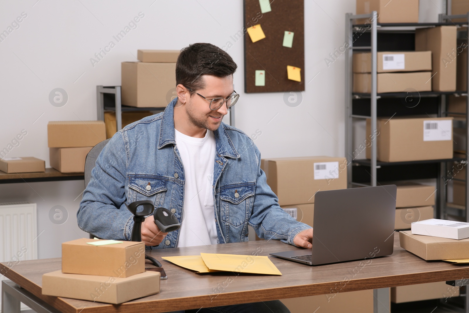 Photo of Seller with scanner, parcels and laptop at table in office. Online store