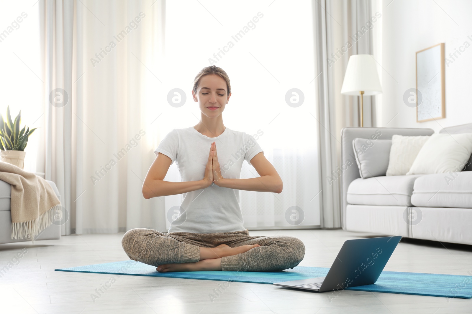 Photo of Woman having online video class via laptop at home. Distance yoga course during coronavirus pandemic