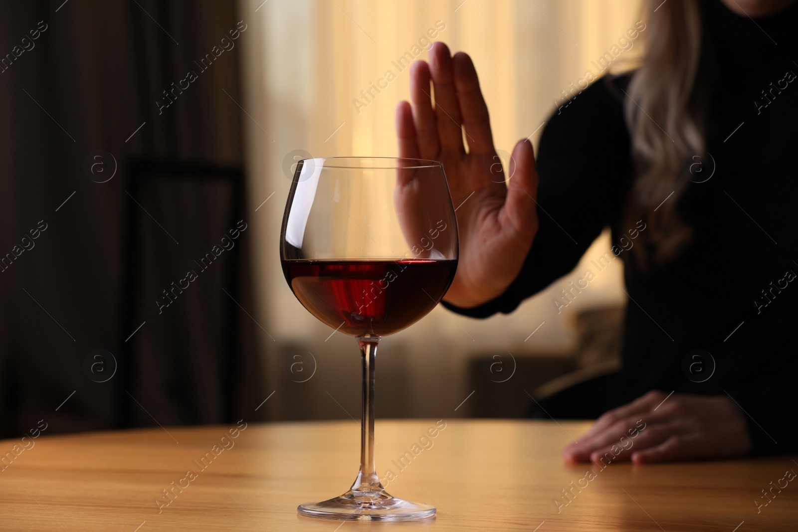 Photo of Woman refusing to drink red wine at home, closeup. Alcohol addiction treatment