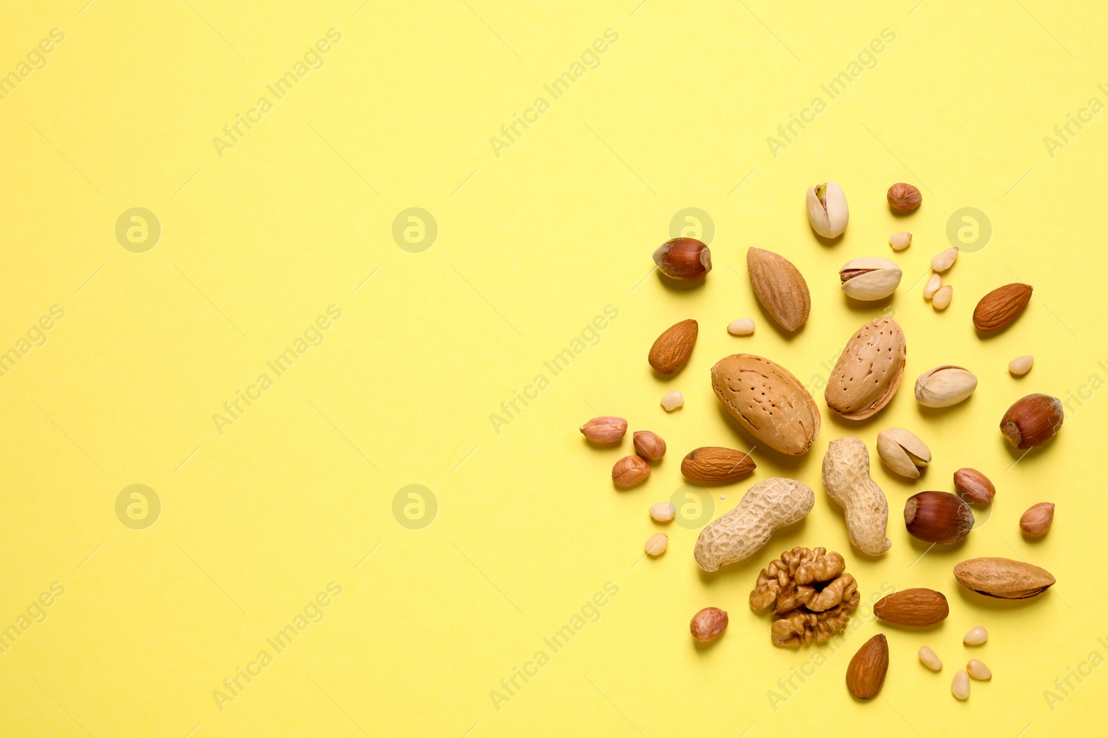 Photo of Different delicious nuts on yellow background, flat lay. Space for text