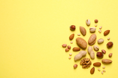 Different delicious nuts on yellow background, flat lay. Space for text