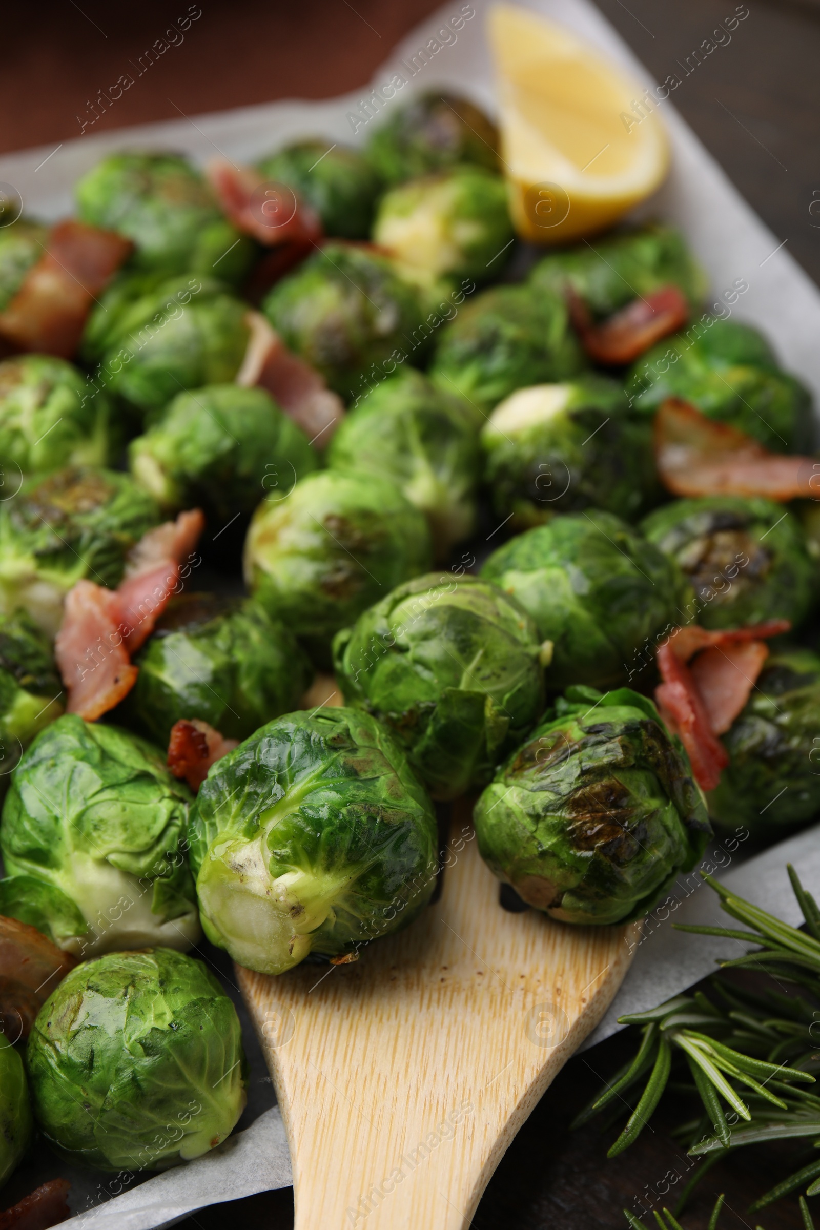 Photo of Delicious roasted Brussels sprouts, bacon and wooden spatula on table, closeup