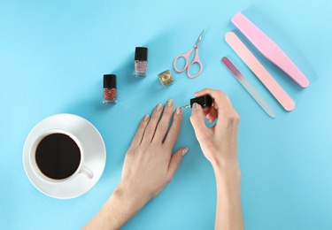 Woman applying nail polish on color background, top view