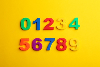 Colorful magnetic numbers on yellow background, flat lay