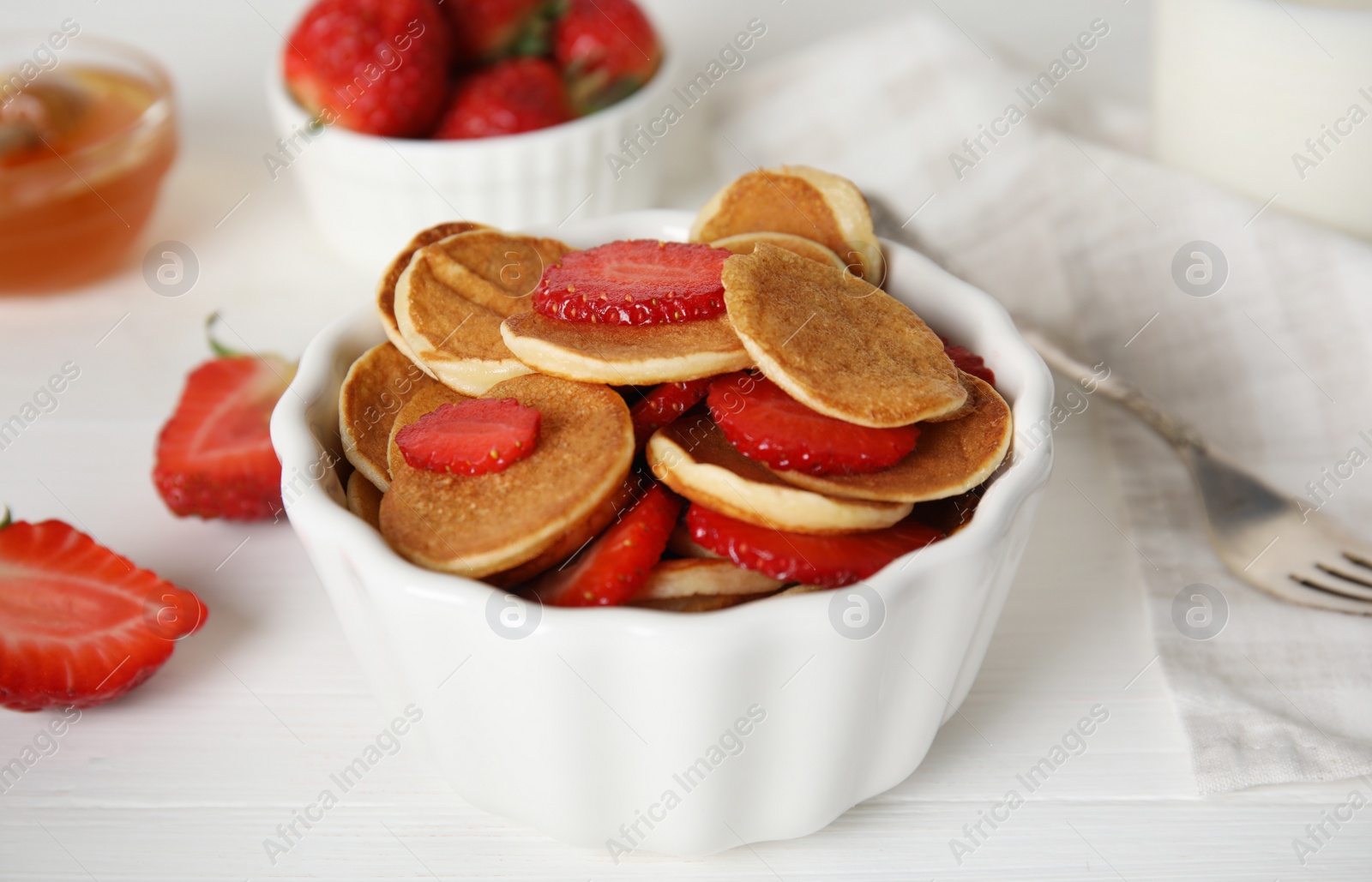 Photo of Delicious mini pancakes cereal with strawberries served on white wooden table