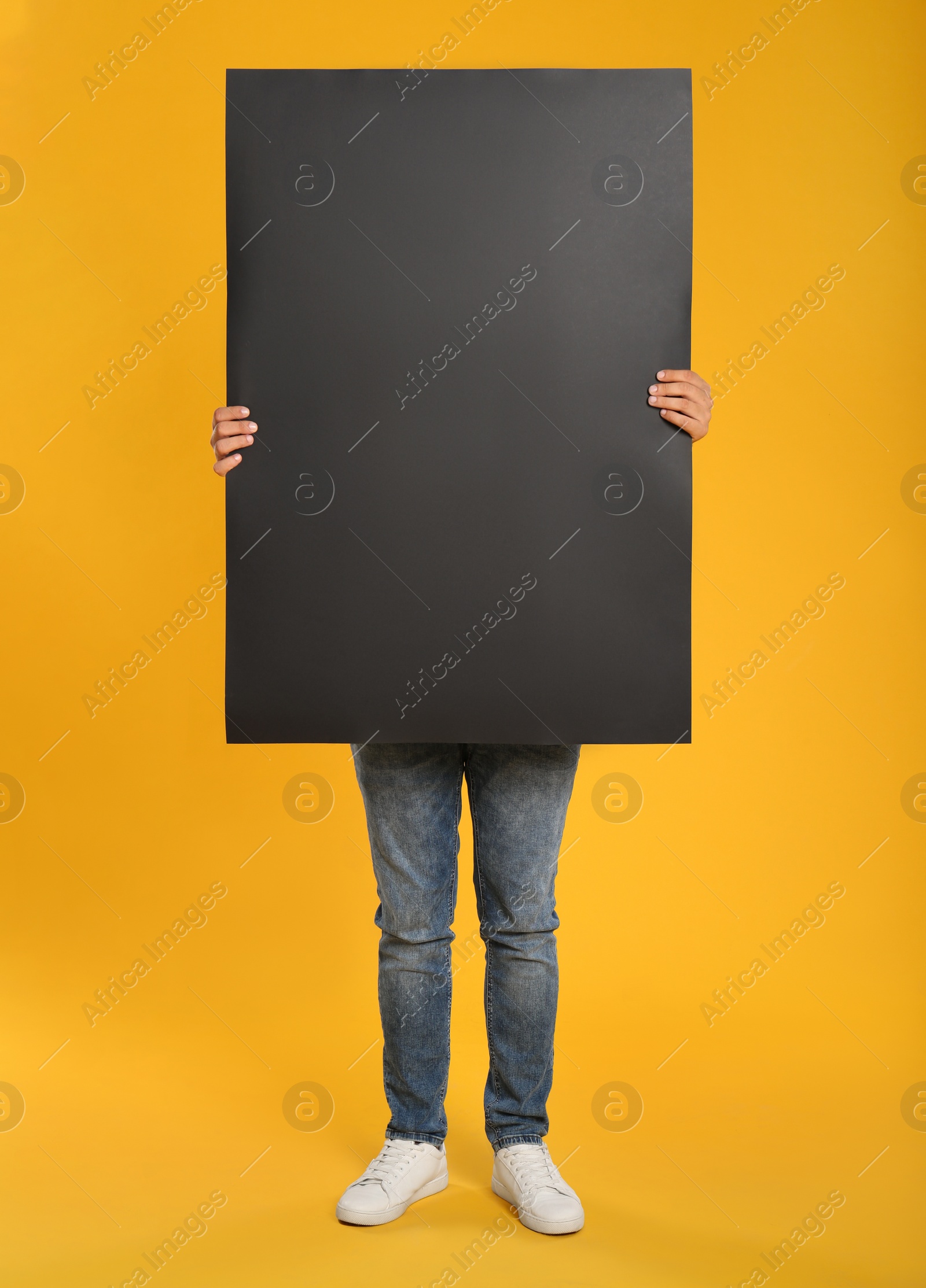 Photo of Man holding black blank poster on yellow background. Mockup for design