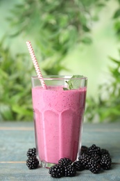 Photo of Tasty fresh milk shake with blackberries on light blue wooden table against blurred background