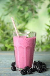 Tasty fresh milk shake with blackberries on light blue wooden table against blurred background