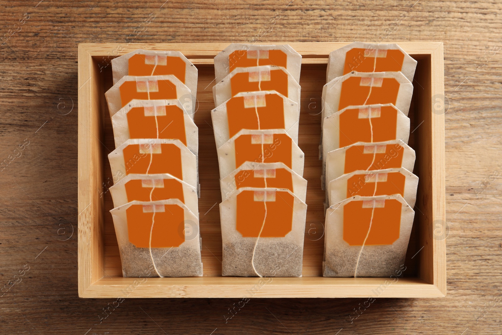 Photo of Paper tea bags with tags in box on wooden table, top view