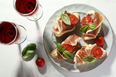 Tasty sandwiches with cured ham, basil and tomatoes on white marble table, flat lay