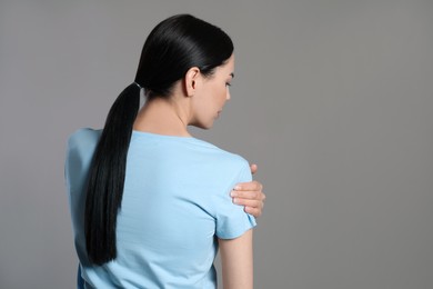 Woman suffering from shoulder pain on beige background, back view