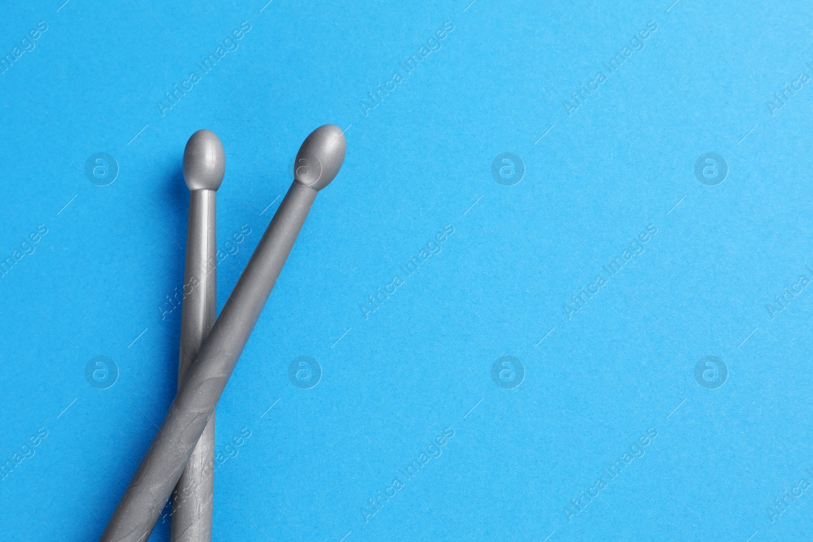 Photo of Two gray drum sticks on light blue background, top view. Space for text