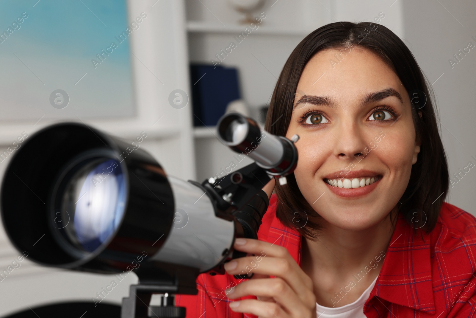 Photo of Beautiful woman using telescope to look at stars in room, closeup