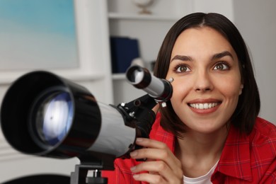 Photo of Beautiful woman using telescope to look at stars in room, closeup