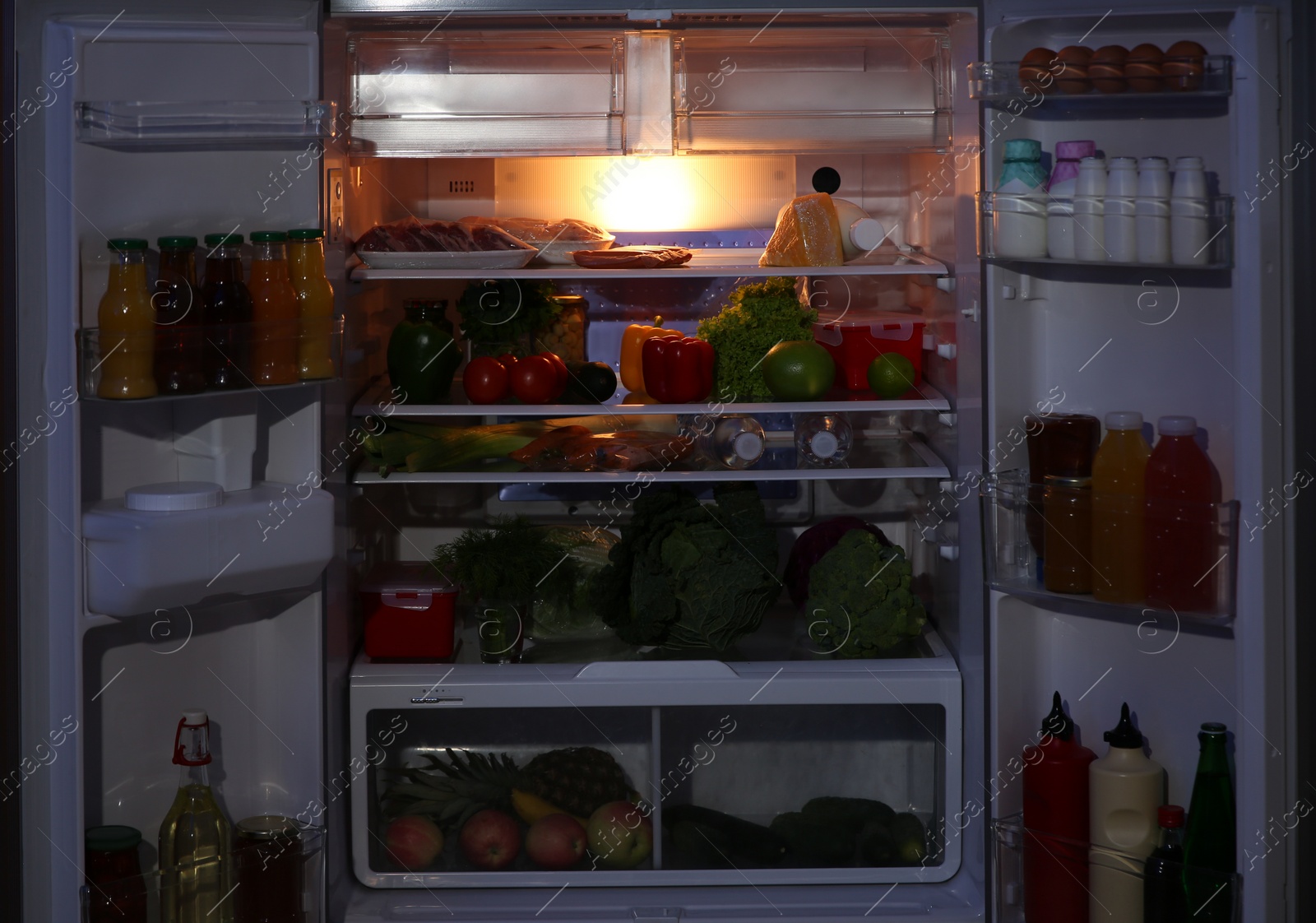 Photo of Open refrigerator filled with food in kitchen at night