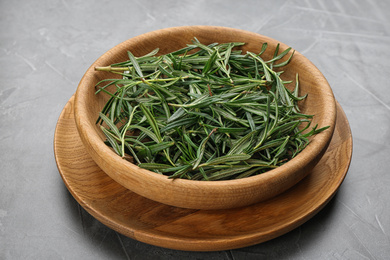 Photo of Fresh rosemary in wooden bowl on grey table