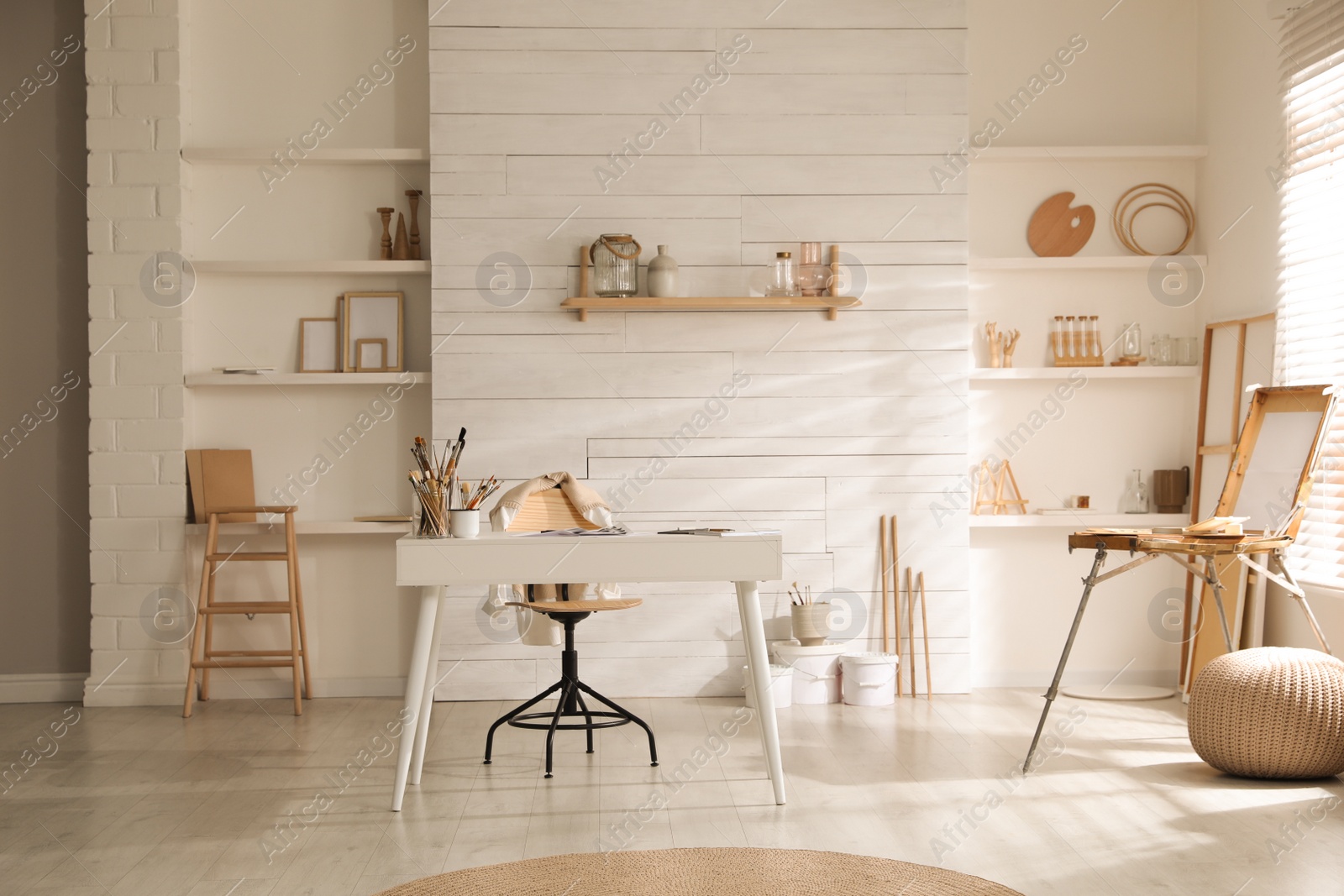 Photo of Modern studio interior with artist's workplace and wooden easel near large window