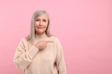 Photo of Portrait of beautiful middle aged woman pointing at something on pink background, space for text