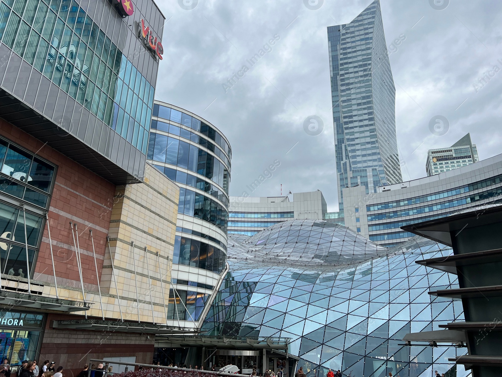 Photo of WARSAW, POLAND - JULY 17, 2022: Big shopping mall and buildings under cloudy sky, low angle view