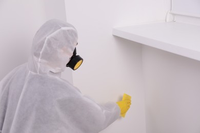 Photo of Woman in protective suit cleaning mold on wall indoors