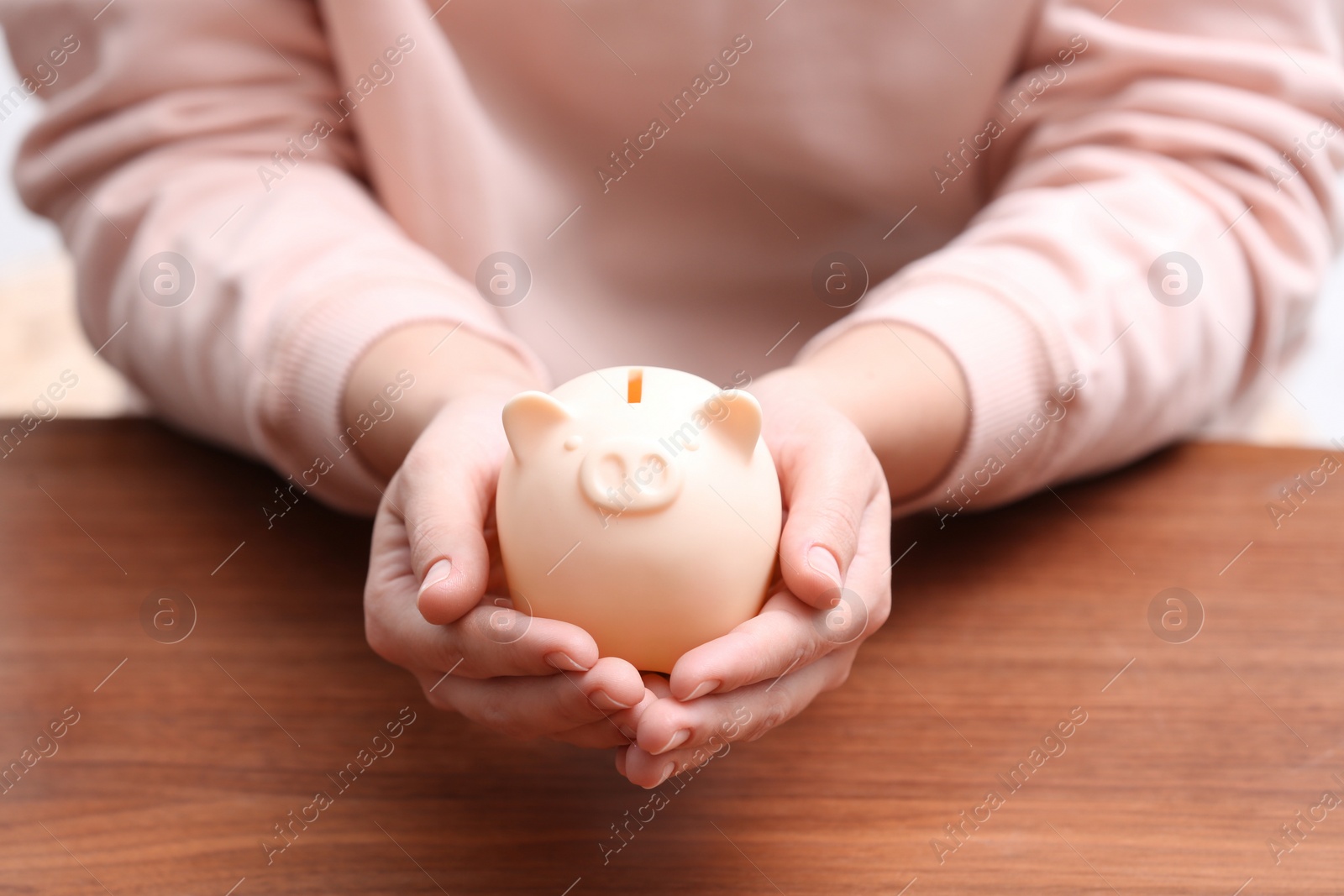 Photo of Woman with piggy bank at wooden table, closeup