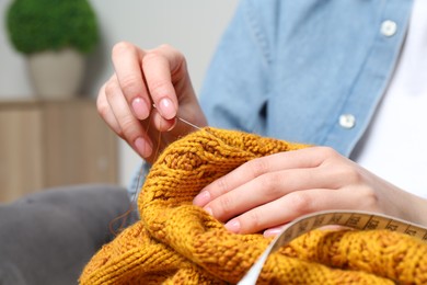 Photo of Woman sewing sweater with needle at home, closeup