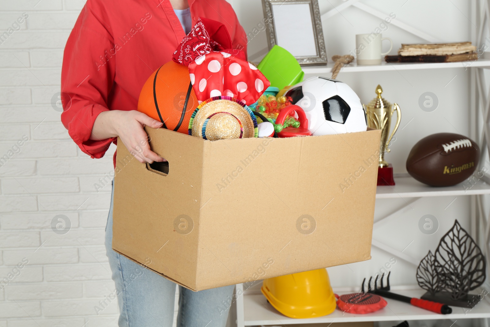 Photo of Woman holding box of unwanted stuff indoors, closeup