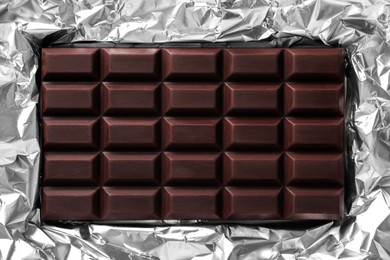 Photo of Delicious dark chocolate bar on foil, top view