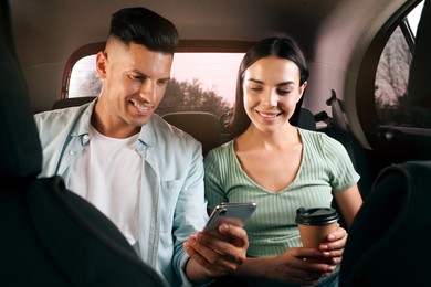 Photo of Happy couple with smartphone and cup of drink in modern taxi