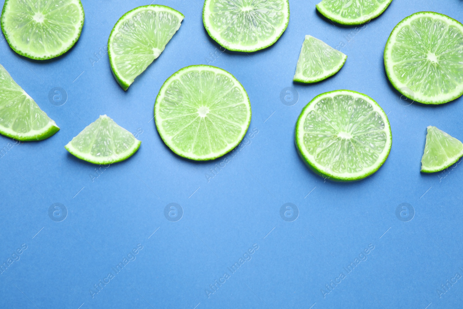 Photo of Juicy fresh lime slices on blue background, flat lay. Space for text