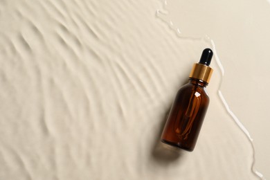 Photo of Bottle of cosmetic oil in water on beige background, top view. Space for text