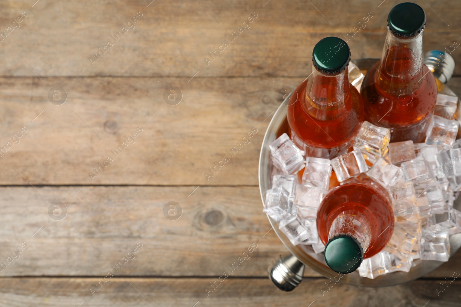 Photo of Metal bucket with beer and ice cubes on wooden background, top view. Space for text