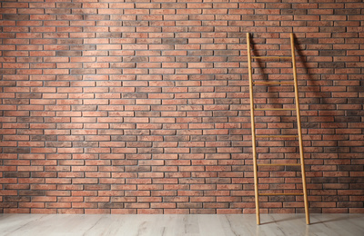 Modern wooden ladder near brick wall. Space for text