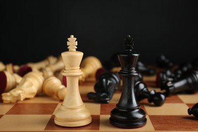 Kings among fallen chess pieces on chessboard against black background, closeup. Competition concept