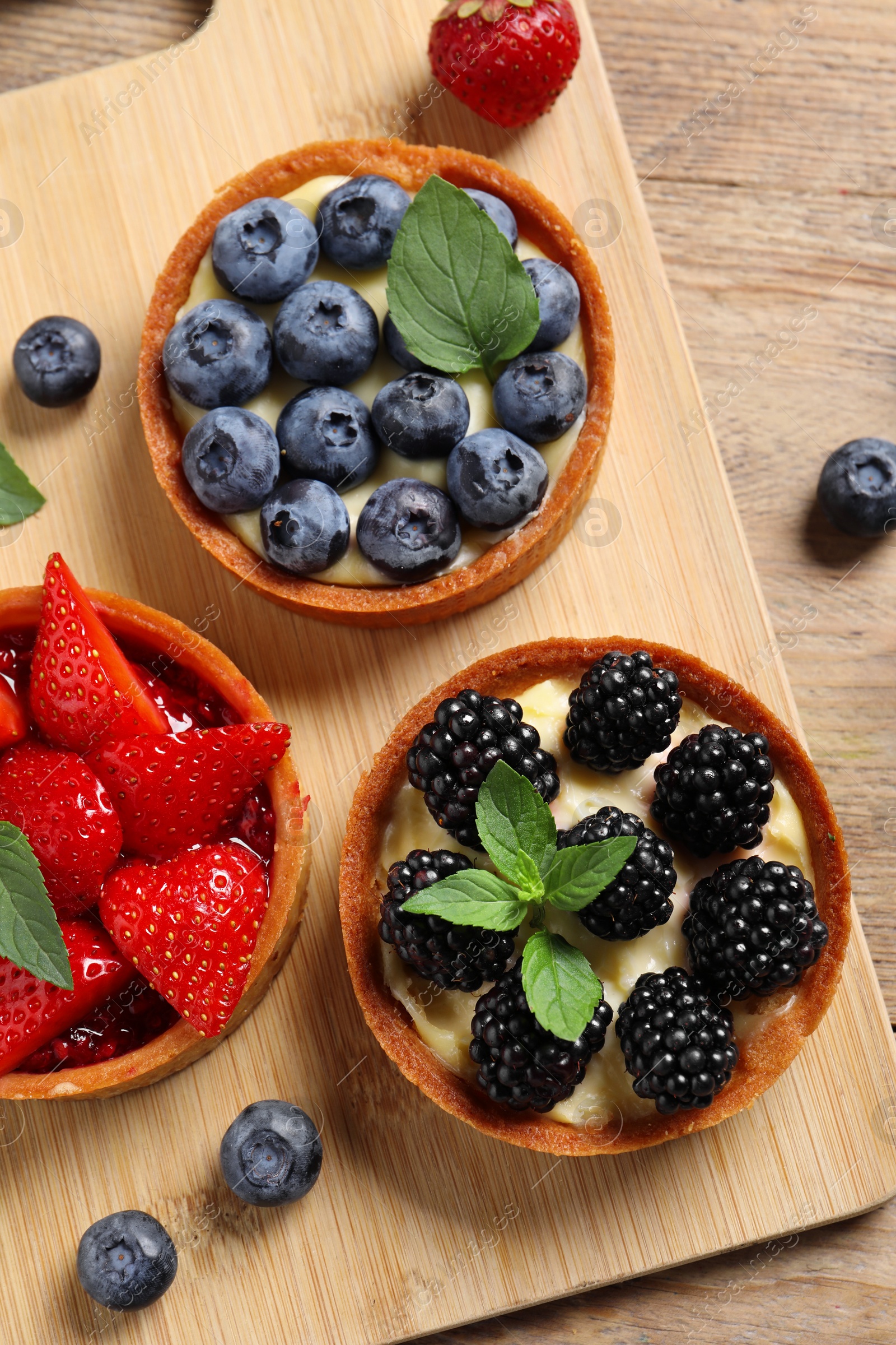 Photo of Tartlets with different fresh berries on wooden table, flat lay. Delicious dessert