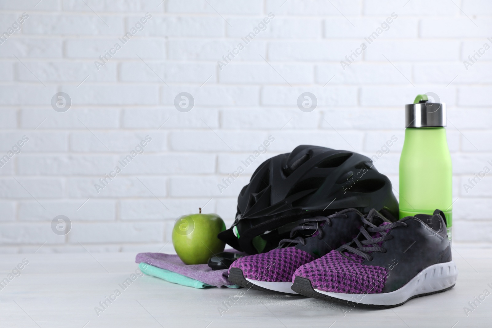 Photo of Different cycling accessories on white wooden table against brick wall, space for text