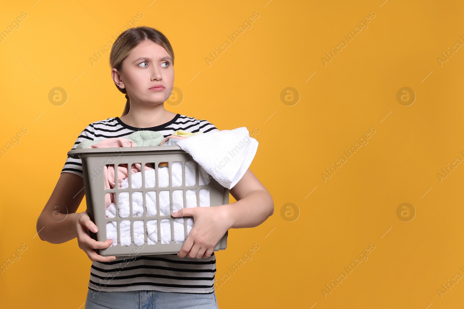 Photo of Sad woman with basket full of laundry on orange background. Space for text