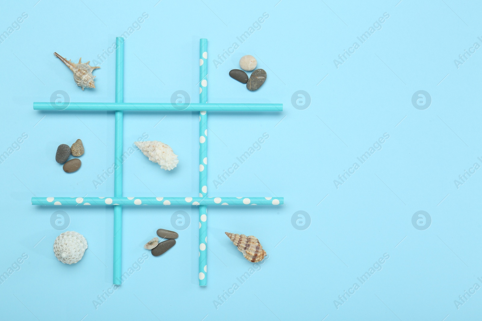 Photo of Tic tac toe game made with sea treasures on light blue background, top view