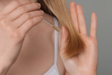 Woman applying essential oil onto hair on grey background, closeup