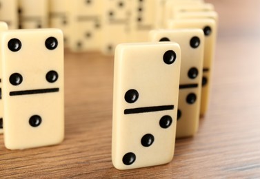 Photo of White domino tiles with black pips on wooden table, closeup