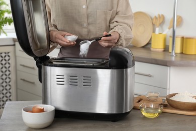 Photo of Making dough. Woman adding salt into breadmaker machine at wooden table in kitchen, closeup