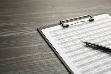 Photo of Clipboard with accounting document and pen on wooden table, closeup. Space for text