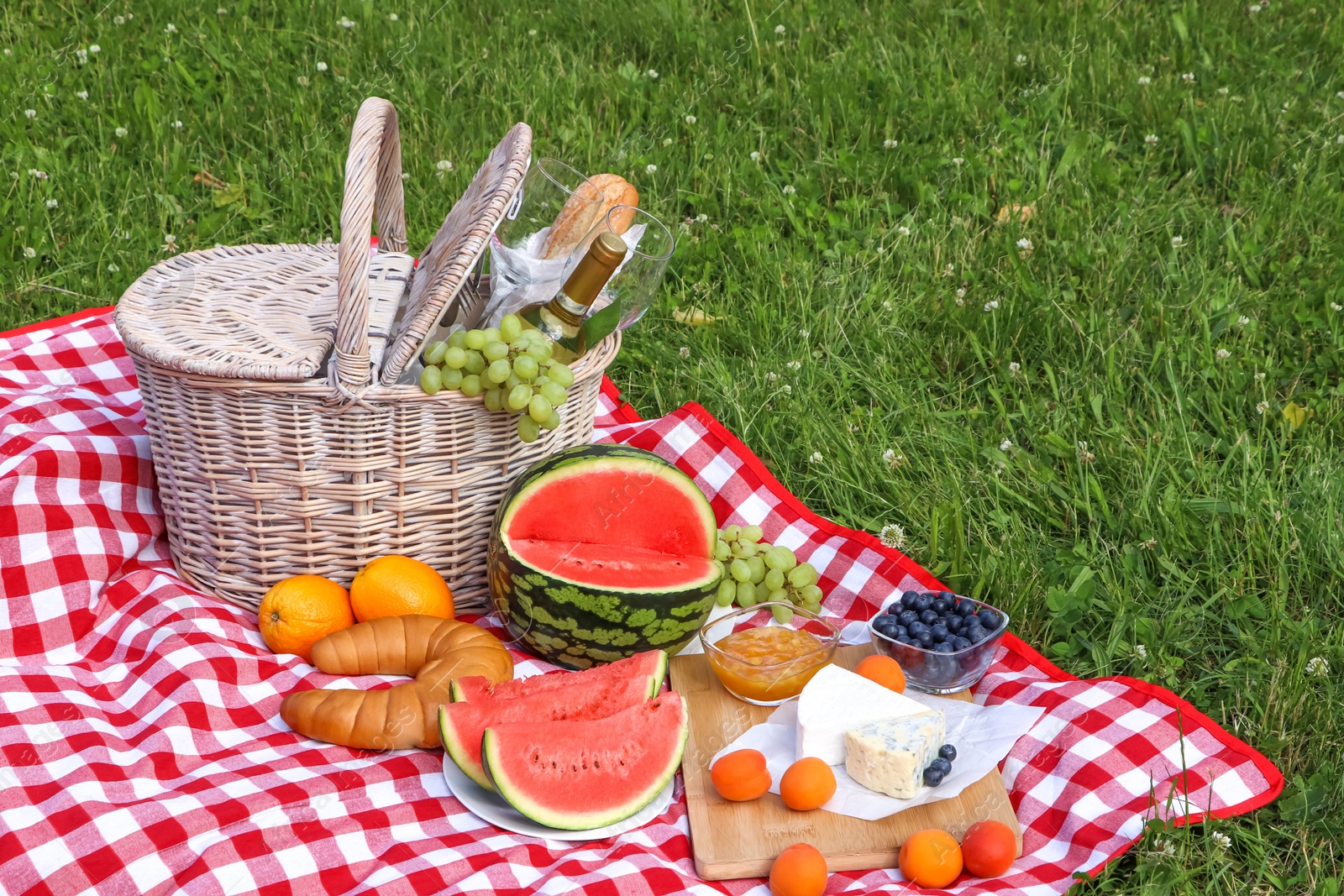 Photo of Picnic blanket with delicious food and wine outdoors on summer day, space for text