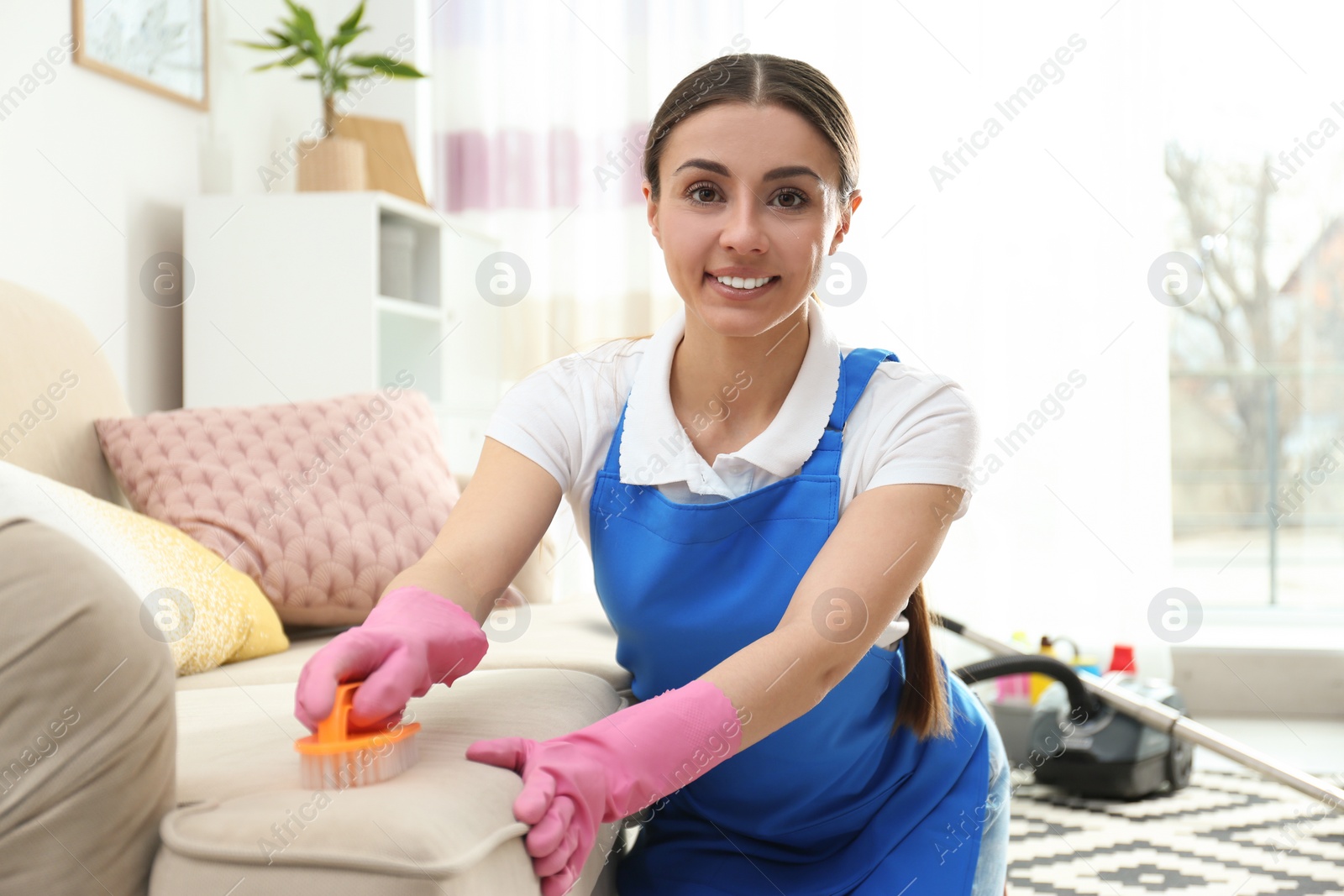 Photo of Portrait of woman cleaning sofa with brush in living room