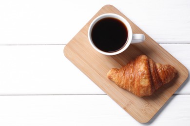 Photo of Tasty breakfast. Cup of coffee and croissant on white wooden table, top view. Space for text