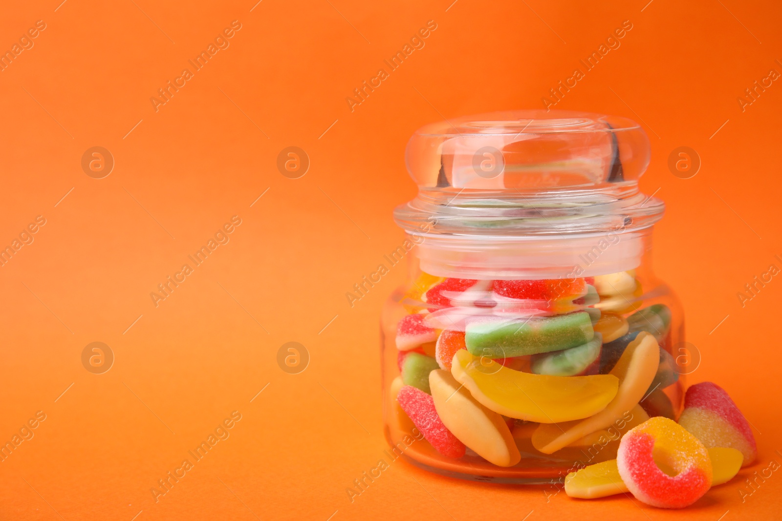 Photo of Tasty jelly candies in jar on orange background, closeup. Space for text